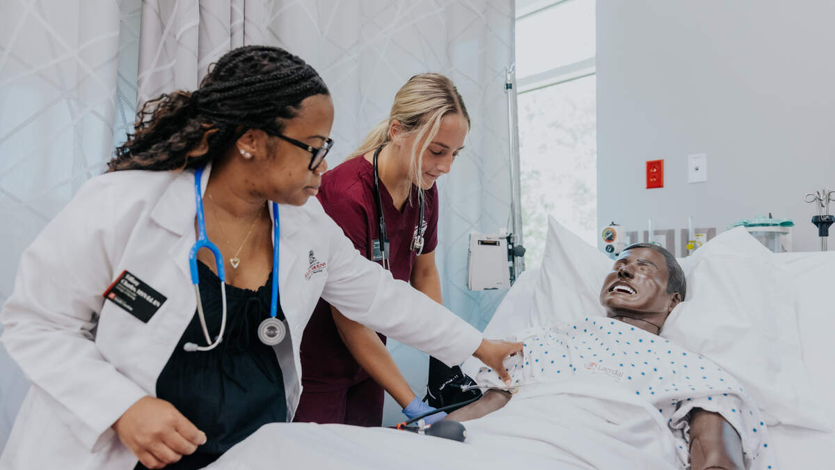 Two female healthcare professionals examining a patient in a hospital bed using medical equipment.